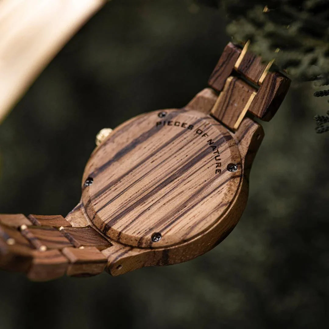 Close-up of a wooden watch with engraved back and striped wood grain pattern outdoors