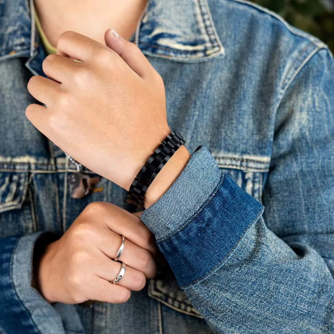 Black metal bracelet on wrist, person in denim jacket, silver rings, casual style