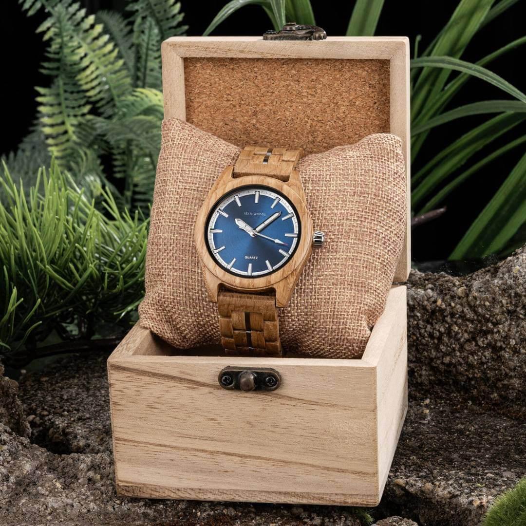 Wooden wristwatch with blue dial in a wooden box surrounded by green plants
