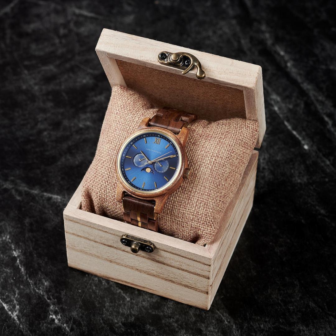 Wooden wristwatch with blue dial in open wooden box on black marble surface