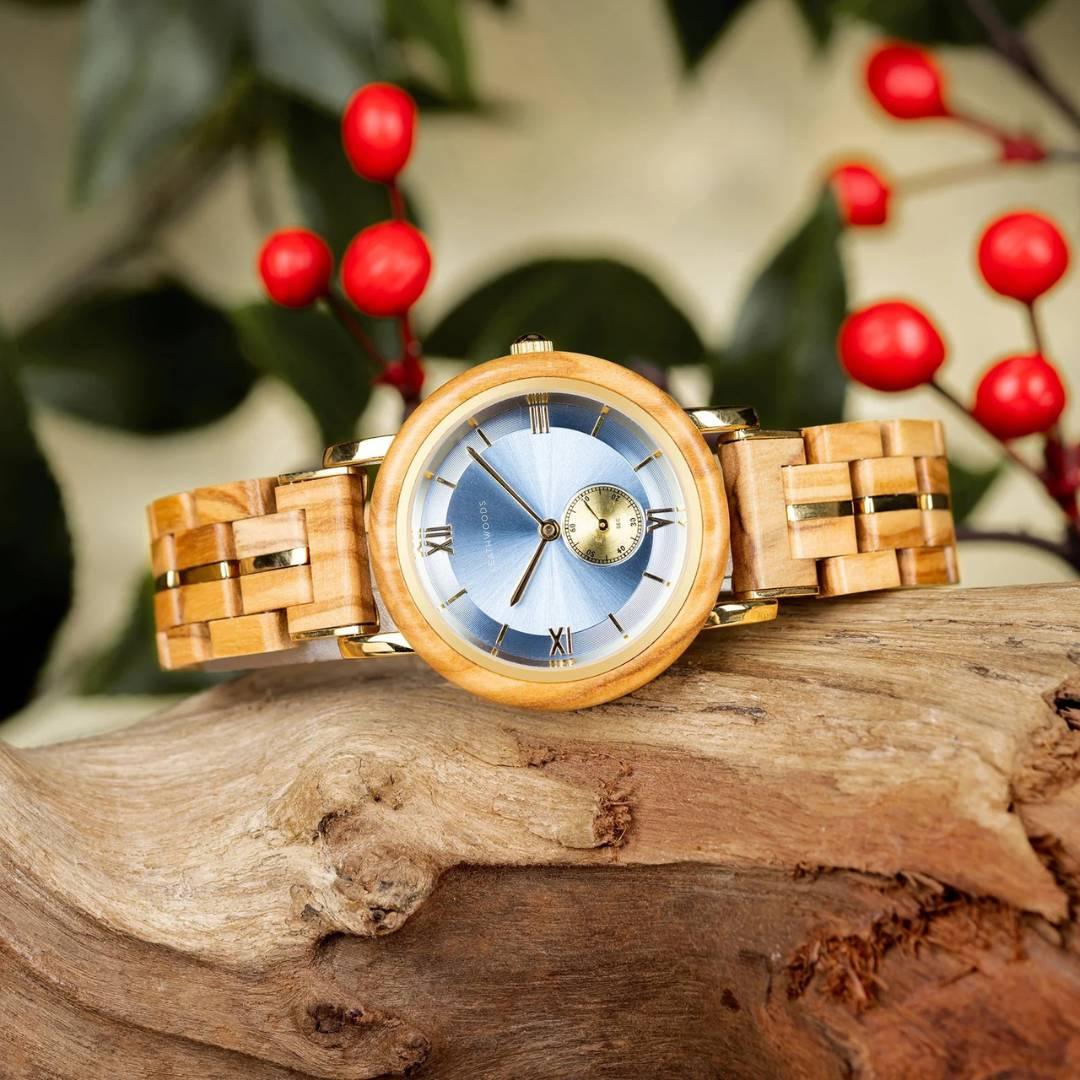 Wooden wristwatch with blue dial on driftwood, red berries and green leaves in background