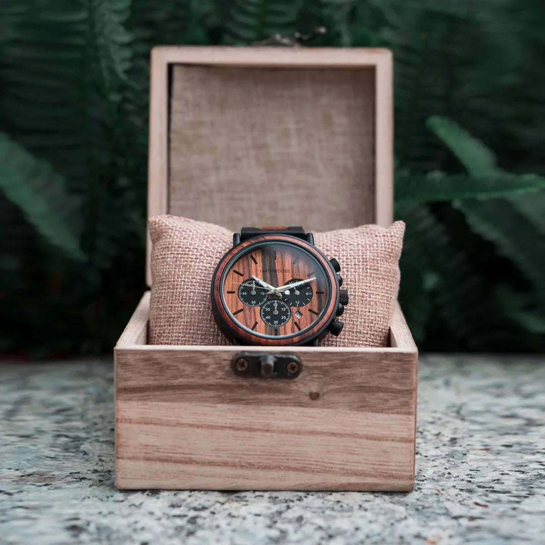 Wooden chronograph wristwatch in a pine gift box on stone with green ferns background