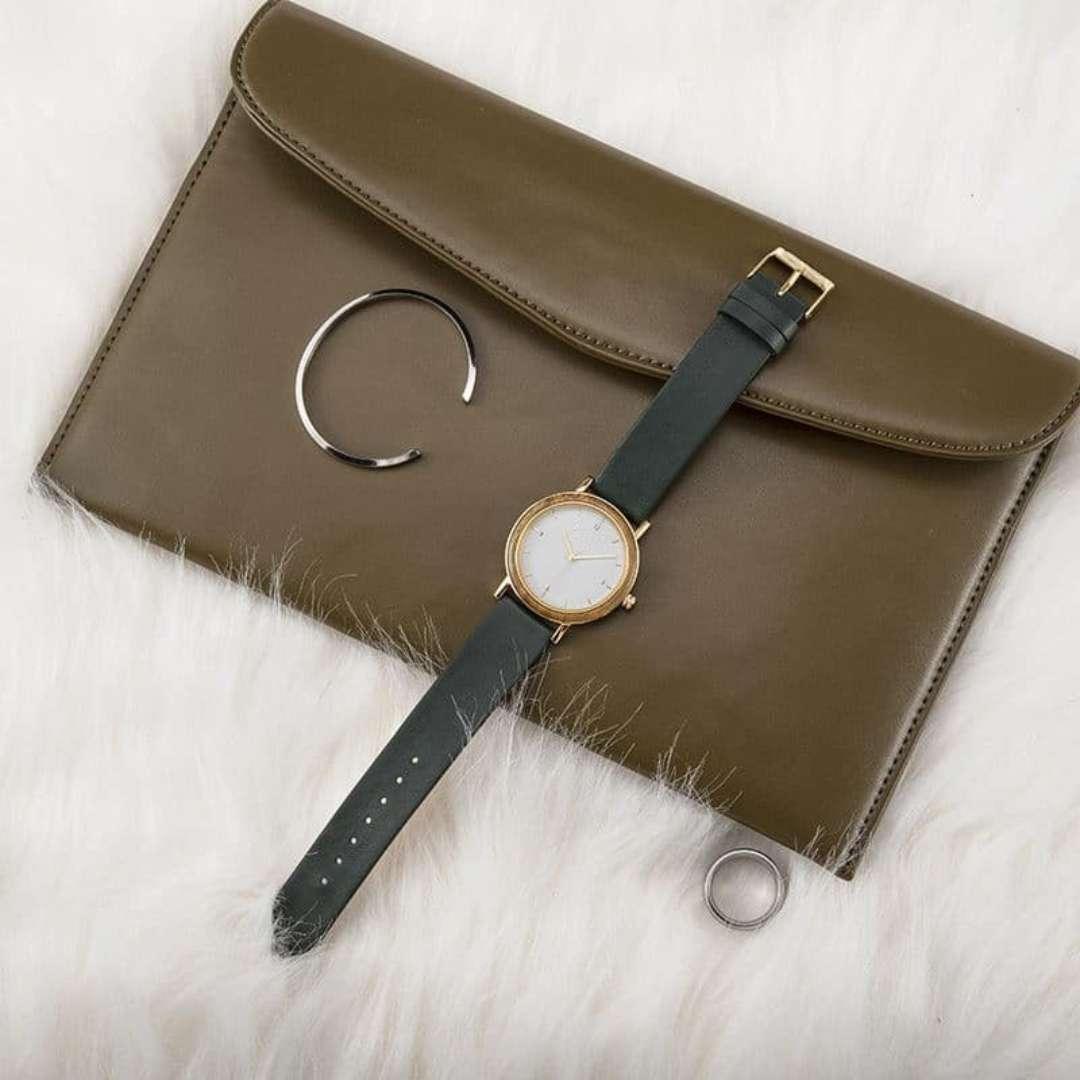 Minimalist gold watch, silver bracelet, ring, and olive clutch on white faux fur