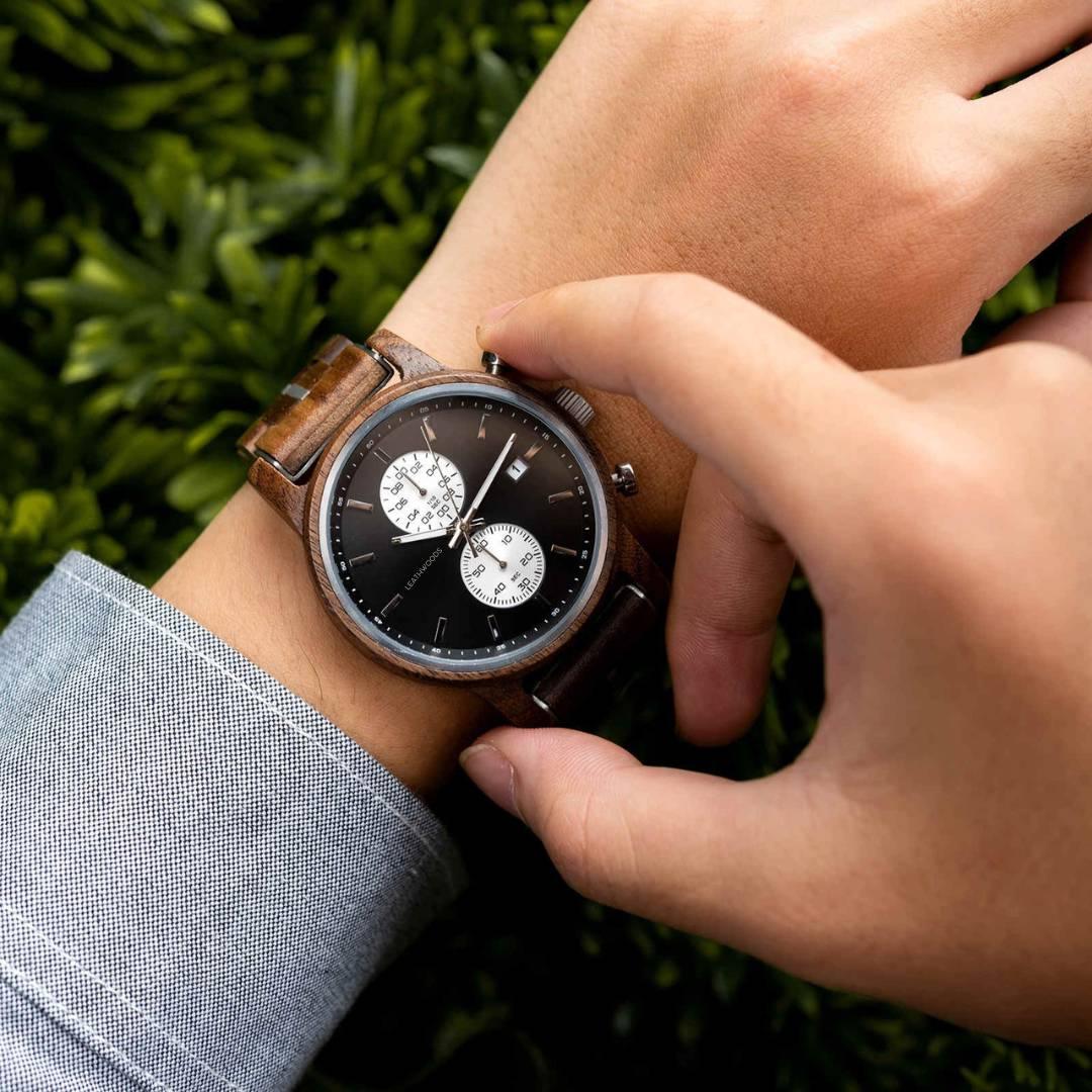 Hand adjusting wooden chronograph wristwatch with black face and white subdials outdoors