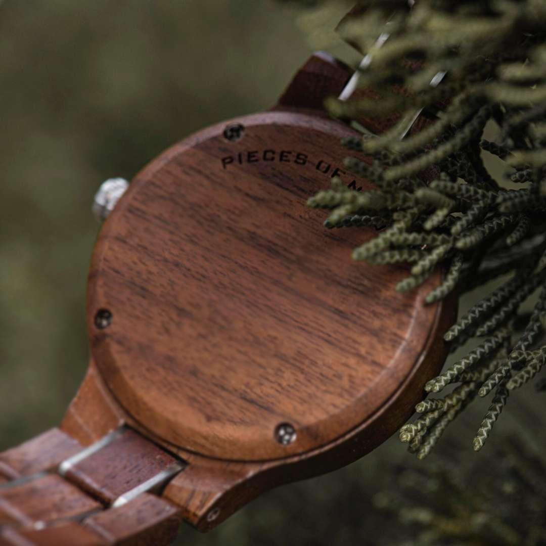 Close-up of a wooden wristwatch backplate partially covered by green leaves outdoors