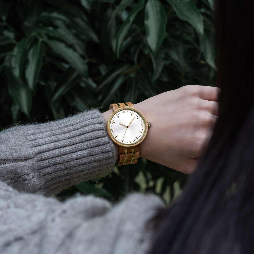 Woman wearing wooden wristwatch with natural band outdoors, green leaves background
