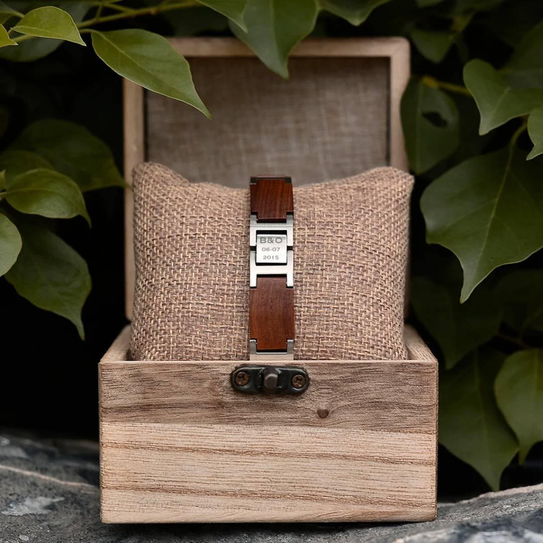 Engraved wooden and metal bracelet in rustic wooden box, surrounded by green leaves