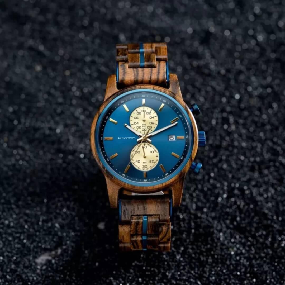 Wooden wristwatch with blue dial, gold markers, chronograph, and date on textured black surface