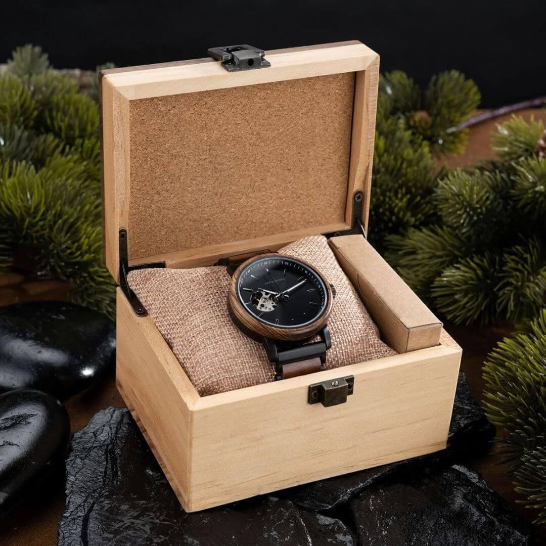 Wooden wristwatch with black dial and leather strap displayed in open wooden box with burlap cushion