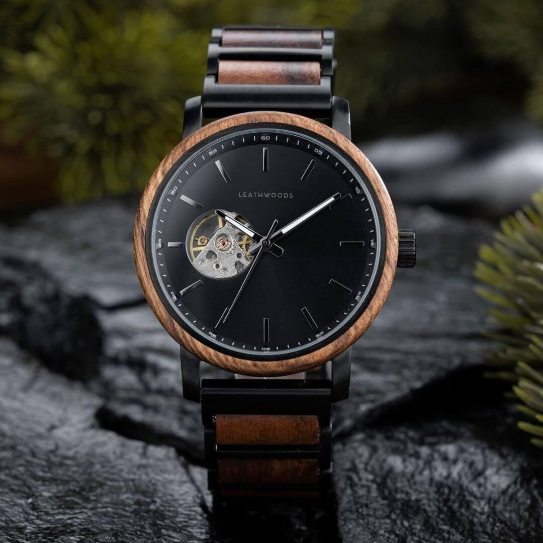 Leathwoods wristwatch with black dial, wooden bezel, and leather strap on dark stone surface