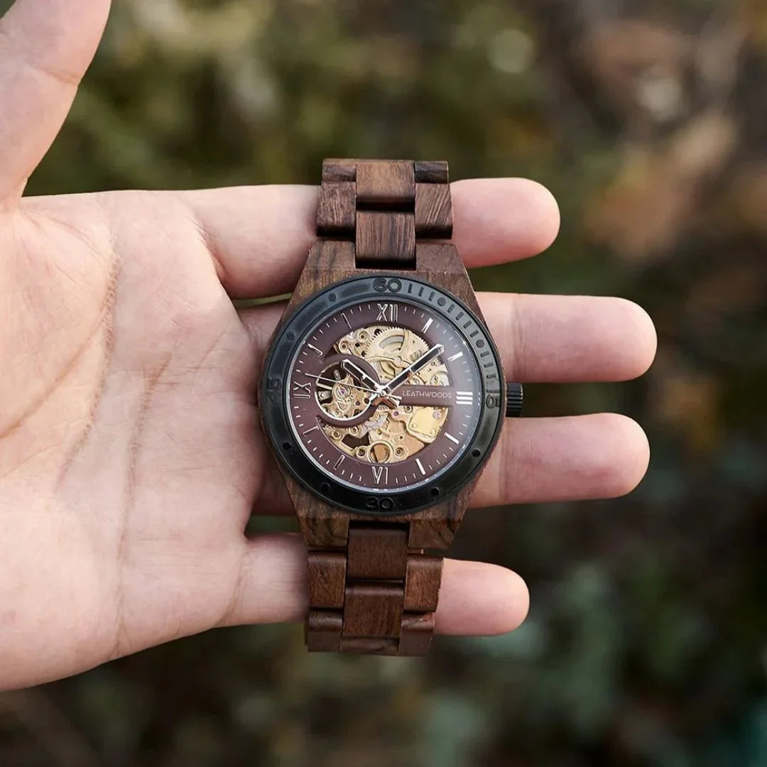 Hand holding a wooden skeleton watch with visible gears, dark bezel, and wood link band