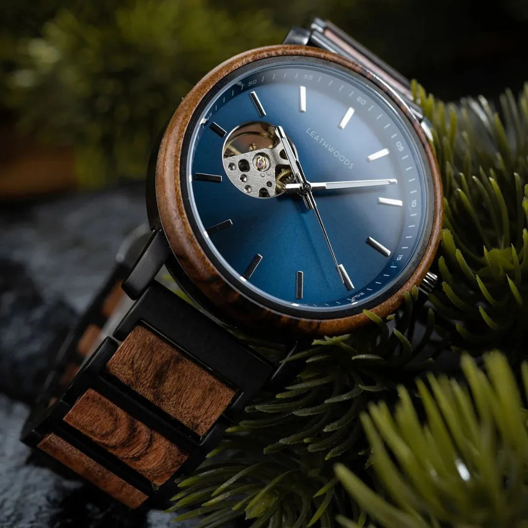 Close-up of a Leathwoods wristwatch with blue dial, wooden bezel, and wood-metal strap on green foliage