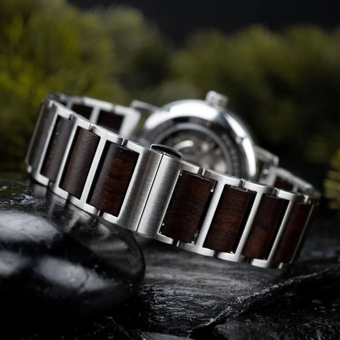close-up of stainless steel and dark wood watch band on black stone surface with blurred background