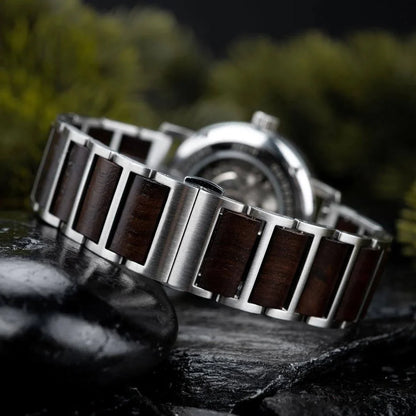 close-up of stainless steel and dark wood watch band on black stone surface with blurred background