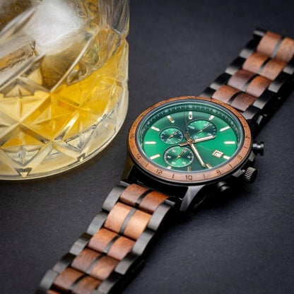 men's chronograph wristwatch with green dial and wood inlay band beside glass of whiskey on black surface