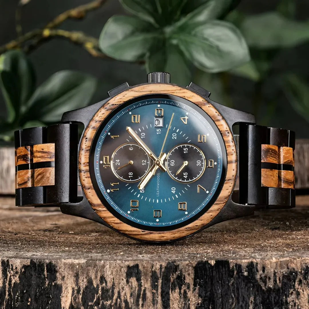 Men's wood and metal chronograph watch with blue face on tree stump, plants in background