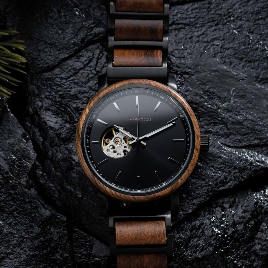 Leathwoods wristwatch with wooden bezel and band, black dial, and exposed gear detail on dark textured background