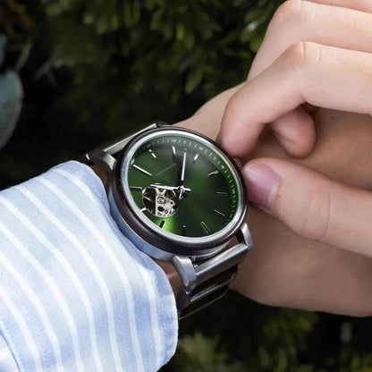 Close-up of wristwatch with green dial and visible gears, worn on wrist with blue striped shirt