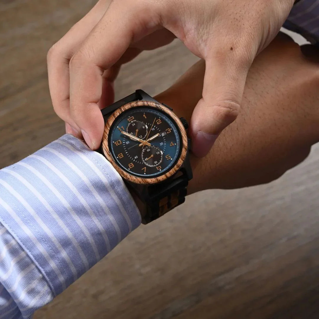 Man wearing a wooden chronograph wristwatch with blue dial, adjusting cuff, on wooden table