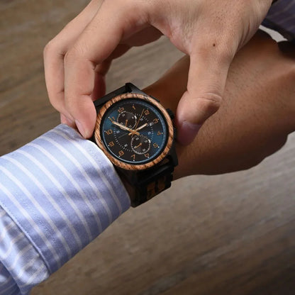 Man wearing a wooden chronograph wristwatch with blue dial, adjusting cuff, on wooden table