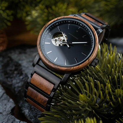 Close-up of Leathwoods black dial wristwatch with wooden bezel and strap on green pine needles