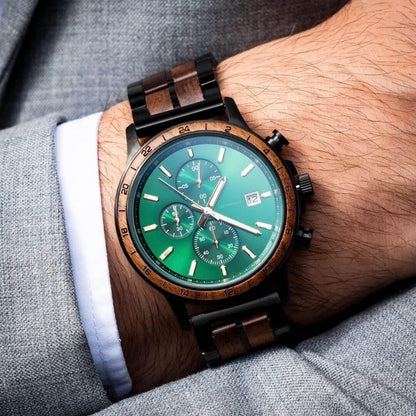 Men's luxury wristwatch with green dial, wooden bezel and band, worn over white cuff and gray suit