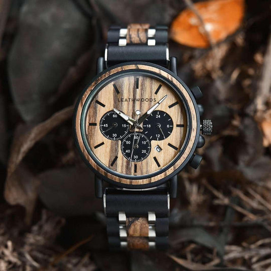 Men's wooden chronograph watch with black subdials on a wood and metal strap, outdoors on leaves