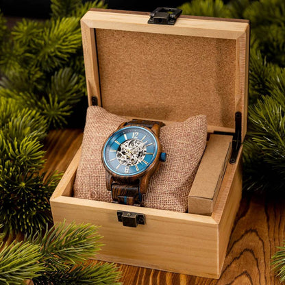 Wooden watch with blue face in a wooden box surrounded by greenery