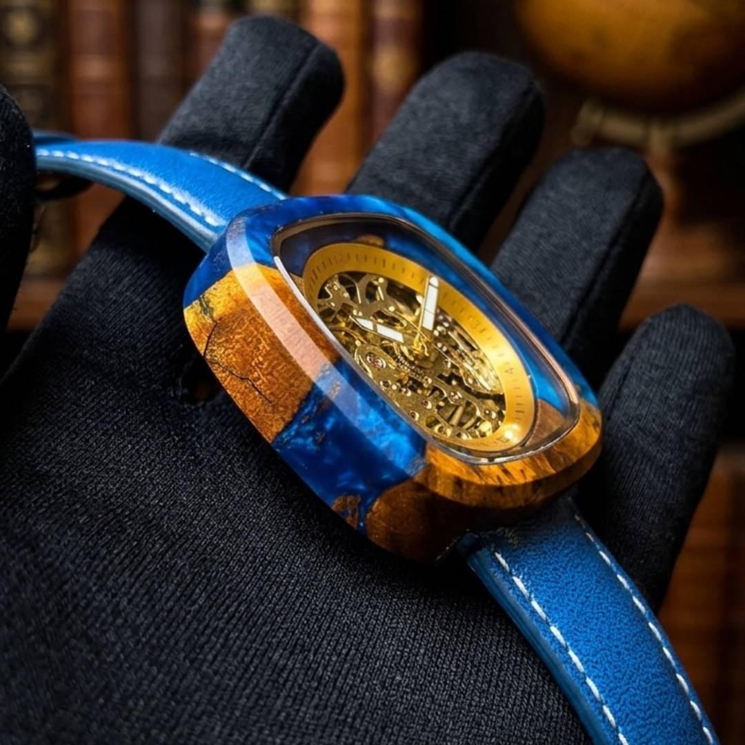 Luxury watch with blue strap and gold face held by a gloved hand against a blurred background
